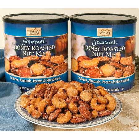 Two cans of Savanna Gourmet Honey Roasted Nut Mix with a plate of nuts in front.