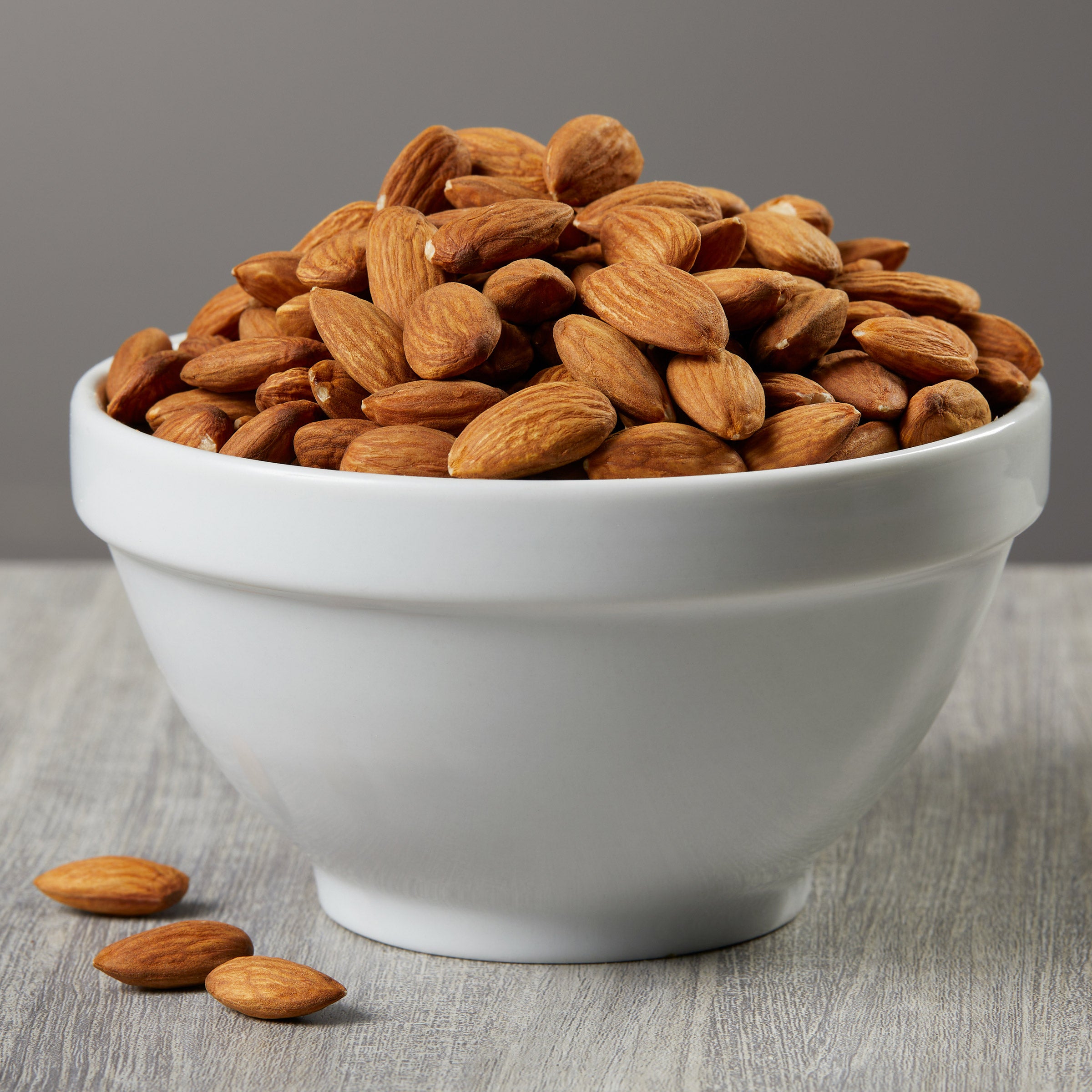 White bowl filled with almonds on a wooden surface