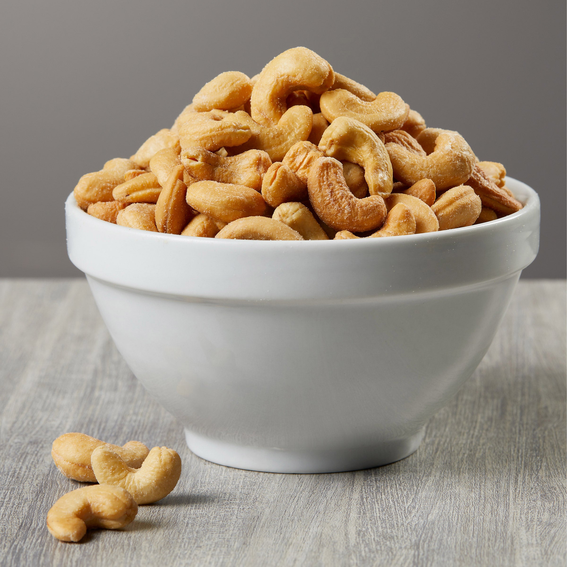 White bowl filled with cashews on a wooden surface