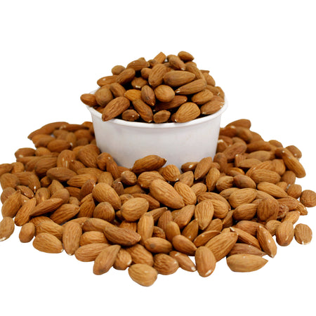 Almonds in a white bowl surrounded by scattered almonds on a white background