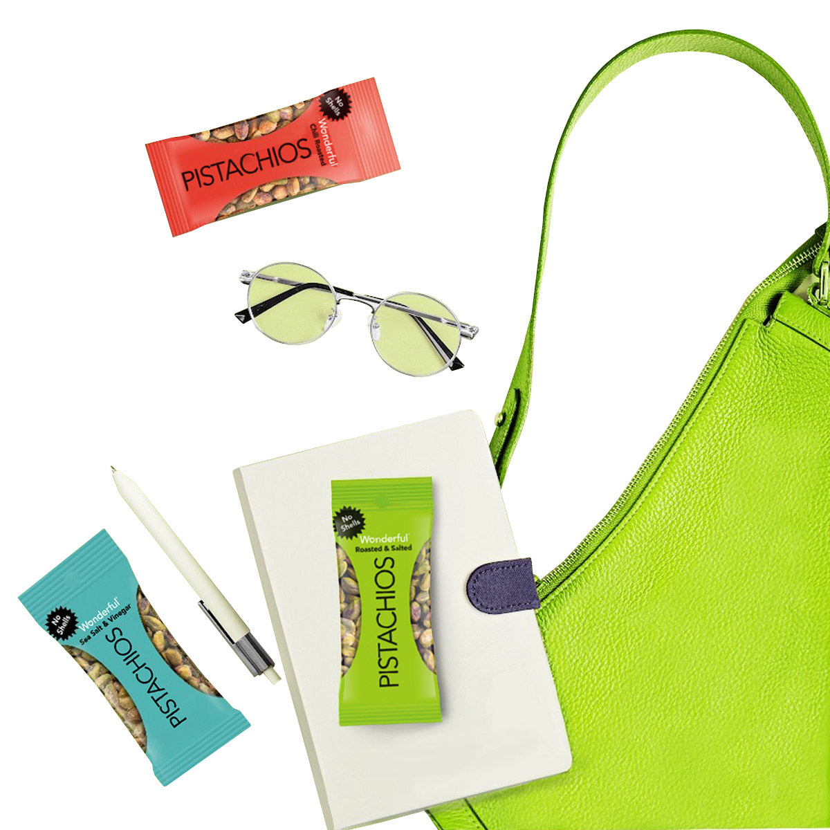 Green handbag with pistachio snacks, sunglasses, and a notebook on a white background