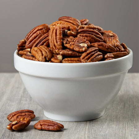 White bowl filled with pecans on a wooden surface
